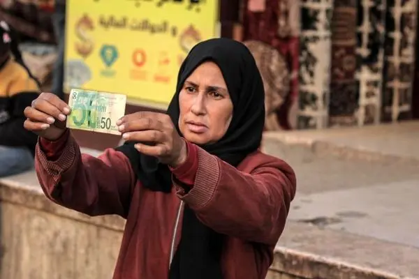 تصاویر؛ زن فلسطینی با ترمیم اسکناس‌های پاره امرار معاش می‌کند